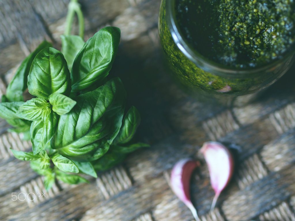 Closeup of fresh Italian basil herb and a glass jasr with home made pesto sauce